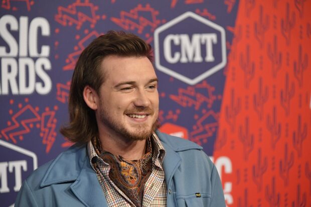 Morgan Wallen smiling at an event wearing a blue jacket and patterned scarf