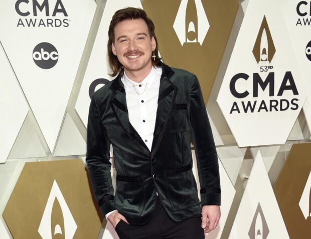 Morgan Wallen standing at the CMA Awards wearing a velvet jacket and white shirt smiling confidently