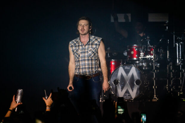 Morgan Wallen wearing a sleeveless plaid shirt performing on stage during a concert