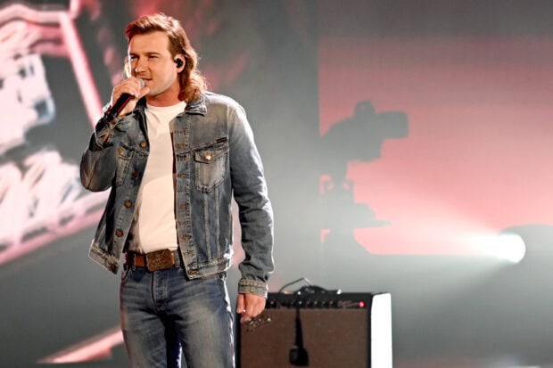 Morgan Wallen singing on stage wearing a denim jacket and jeans