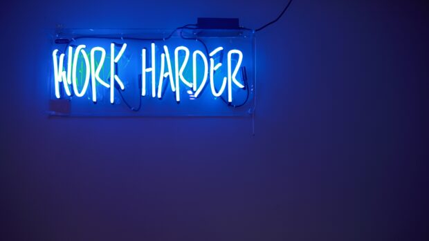Neon sign with motivational phrase work harder glowing in blue light