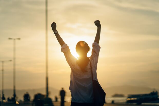 A woman raising her arms in triumph at sunset showing motivation and success