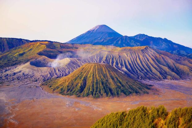 Volcanic landscape of Mount Bromo with smoking crater and surrounding mountains in a vibrant sunrise view