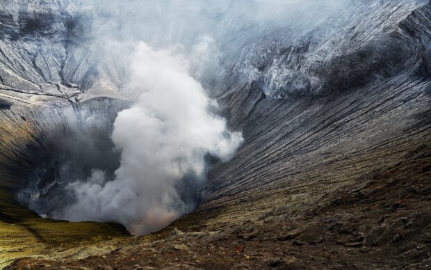 Smoky crater of Mount Bromo emitting white steam surrounded by rocky terrain