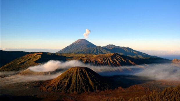 Volcanic landscape with Mount Bromo smoking in the distance and surrounding hills and mist