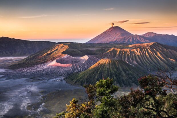 A breathtaking view of Mount Bromo volcano with surrounding mountains and lush greenery at sunrise