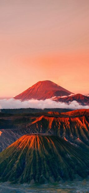 Mount Bromo volcanic landscape illuminated by sunset light with clouds below the peaks