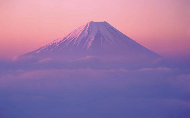 Snow capped Mount Fuji surrounded by clouds during a pink and purple sunset sky