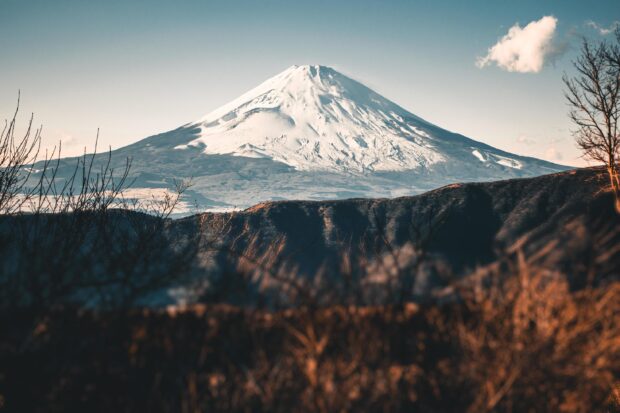 Snow covered Mount Fuji stands tall above autumn landscape with clear sky