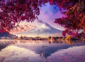 A serene view of Mount Fuji with autumn leaves framing a calm lake and a boat floating in the water