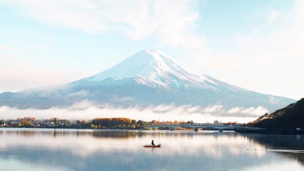 A serene view of Mount Fuji with autumn trees and a person fishing on the lake