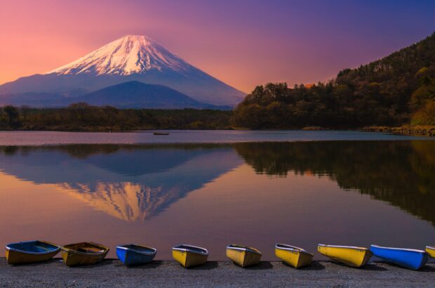 A serene view of Mount Fuji with boats lined up on the shore and the mountain reflected in the calm lake water