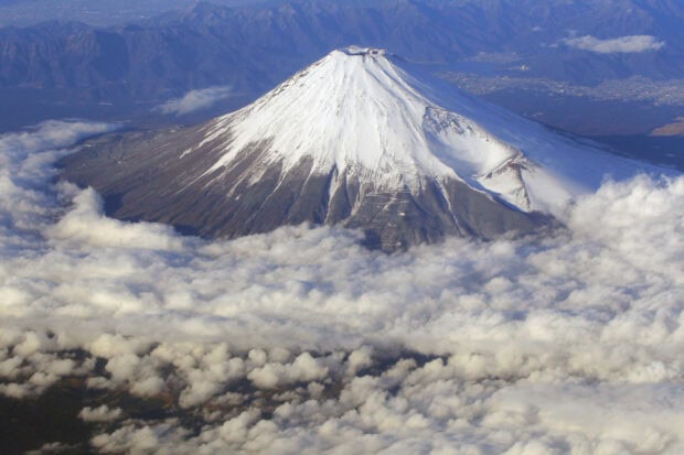 Mount Fuji stands tall above the clouds with a snow capped peak and surrounding mountains