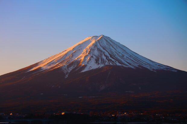 Snow capped Mount Fuji glowing in sunlight during sunset
