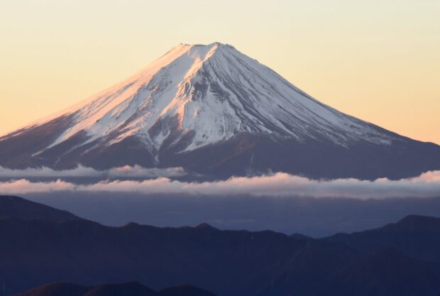 Snow capped Mount Fuji standing above clouds during sunset with clear sky