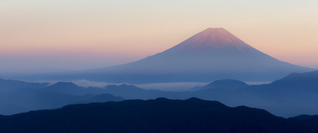 Mount Fuji stands tall over misty mountains during a calm sunrise sky