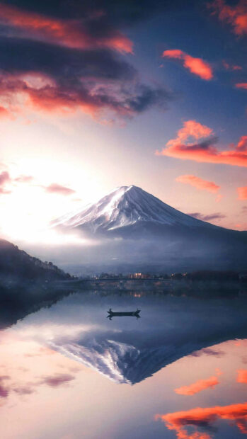 A serene view of Mount Fuji with its reflection on calm water during sunset featuring vibrant clouds