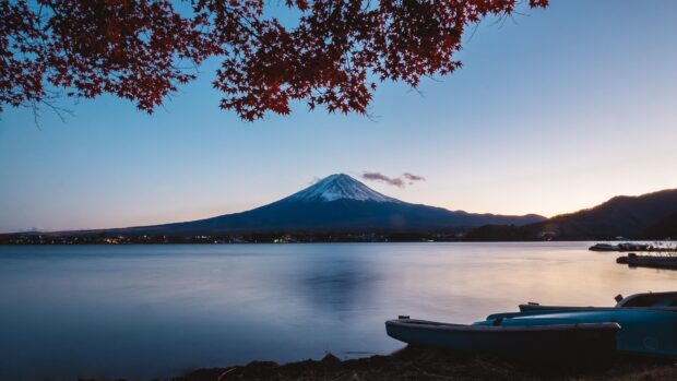 Snow capped Mount Fuji with red autumn leaves reflecting on calm lake at dusk
