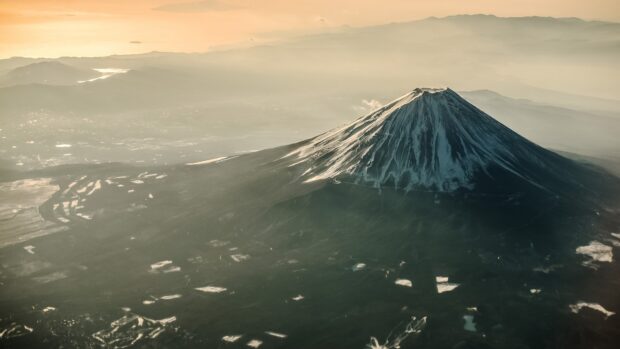 Aerial view of Mount Fuji with snow covering its peak during a hazy sunset