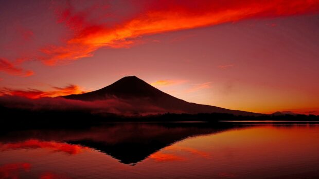 Mount Fuji silhouette reflects on calm lake under vibrant sunset sky