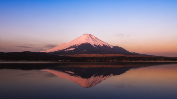 Mount Fuji with snow capped peak reflecting in calm lake waters at sunset