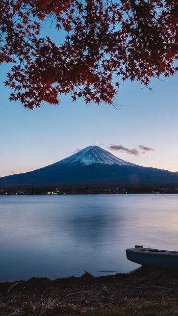 Snow capped Mount Fuji framed by red maple leaves over calm water