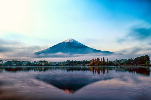A scenic view of Mount Fuji with autumn trees reflected on the calm lake surface