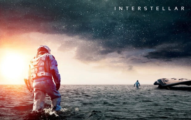 An astronaut from Interstellar walking through water towards a distant spaceship at sunset