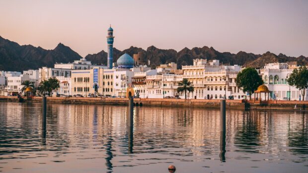 Waterfront view of Muscat Oman city with mountains and a mosque reflecting on calm water