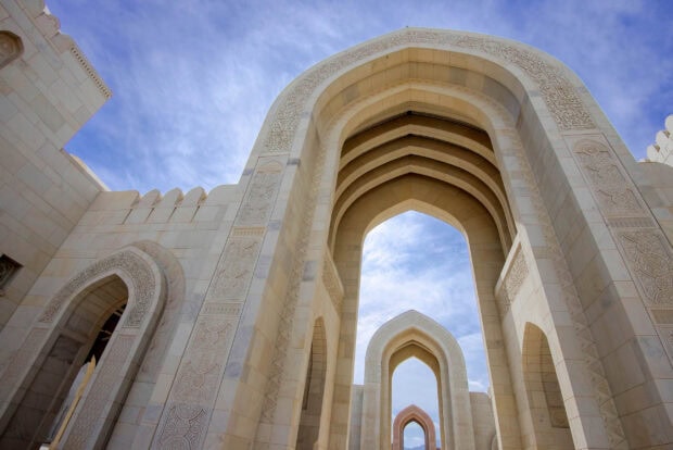 Ornate Muscat architecture with intricate arches against a blue sky
