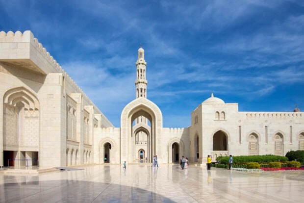 The mosque architecture in Muscat Oman with clear blue sky and people walking around