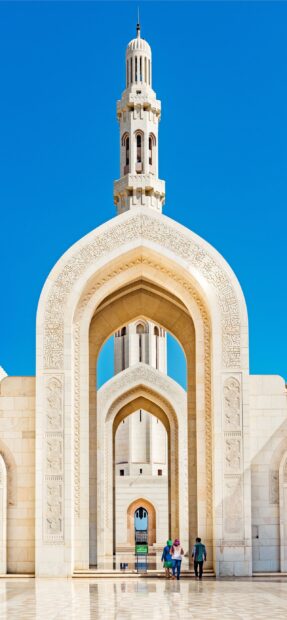 Intricate archways showcasing Muscat architecture with people walking under clear blue sky