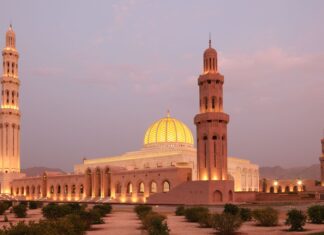 The grand mosque with illuminated dome and tall minarets in Muscat Oman at dusk