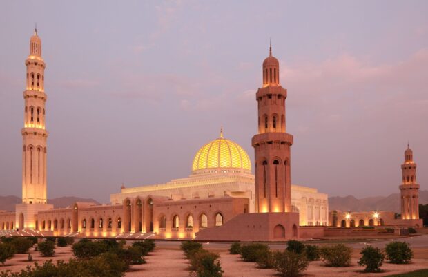 The grand mosque with illuminated dome and tall minarets in Muscat Oman at dusk