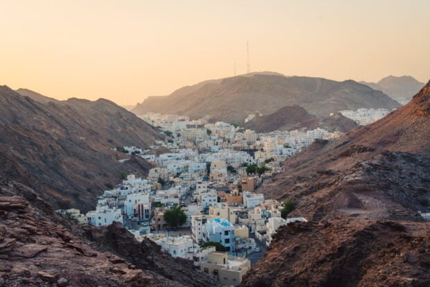 A panoramic view of Muscat city nestled between rocky mountains at sunset