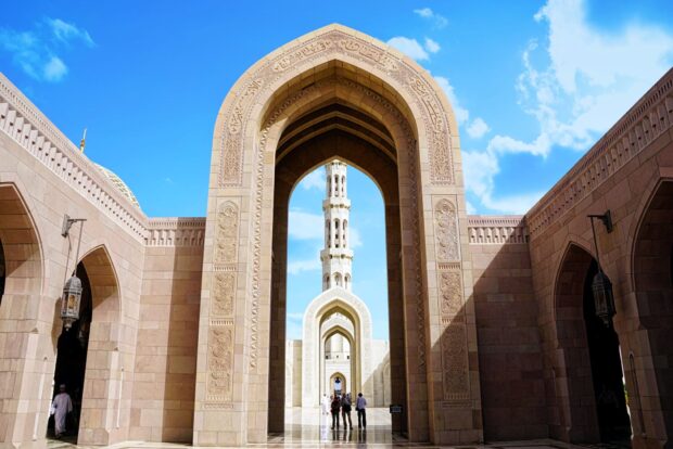 The architecture of Muscat showcasing intricate arches and a tall tower in clear sky