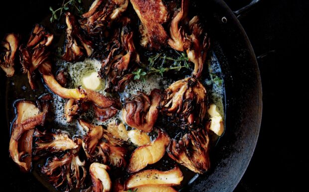 Sautéed mushrooms cooking in butter with herbs in a black pan