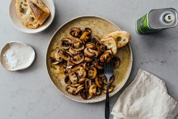 Sautéed mushrooms served on a plate with bread slices and seasoning displayed on the table