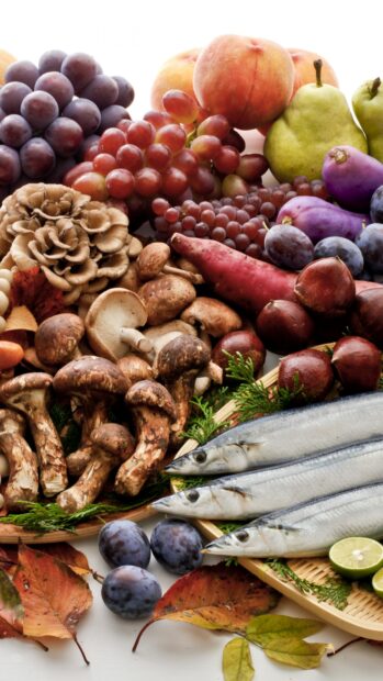 A variety of mushrooms surrounded by fruits and fish on a white surface