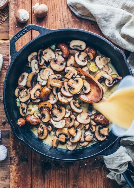 Sliced mushrooms cooking in a cast iron skillet with broth being poured in