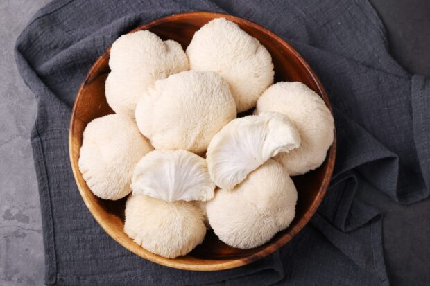 White lion's mane mushrooms arranged in a wooden bowl on dark fabric
