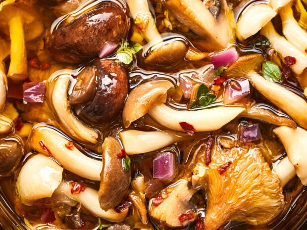 A close up of various mushrooms being marinated with herbs and spices in a glossy liquid