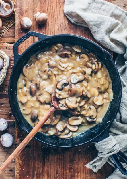 Cooked mushroom slices in creamy sauce in a cast iron skillet on wooden surface