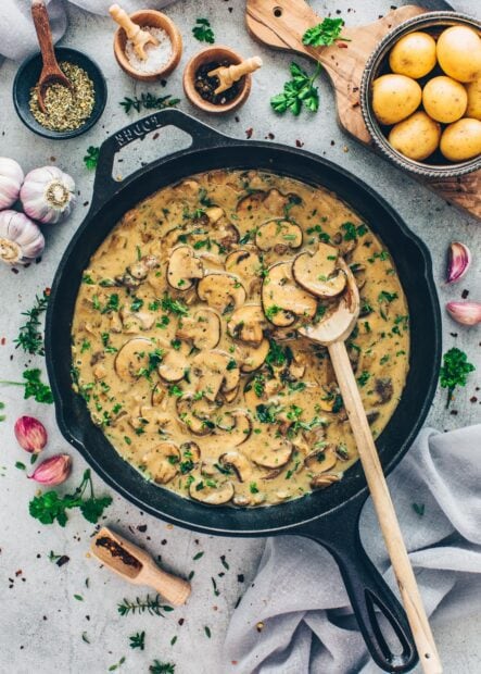 Creamy mushroom sauce with fresh herbs and spices in a skillet with potatoes and garlic nearby