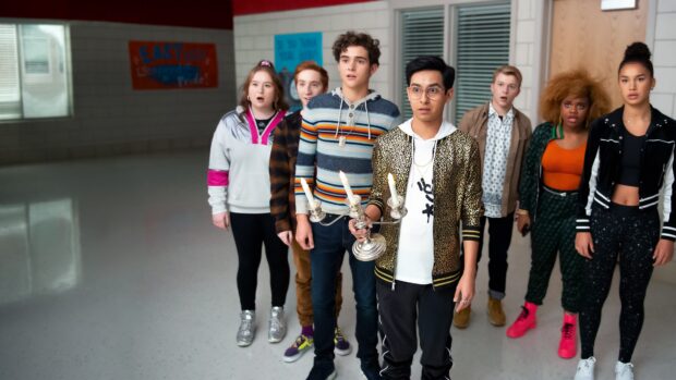 A diverse group of teenagers exploring a school hallway with a candle holder in a musical scene