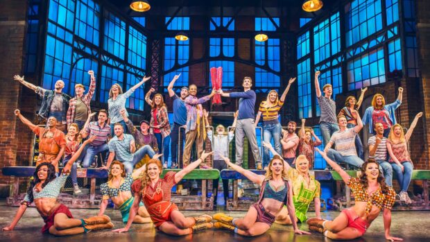 A diverse cast of performers celebrating on stage in a vibrant musical theater scene