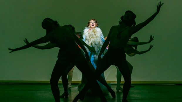 A musical performance featuring a lead singer with dancers striking poses on stage