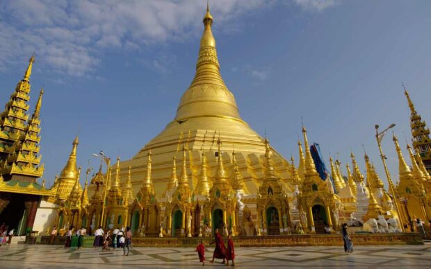 Golden pagoda in Myanmar with monks and visitors under a blue sky at a famous Buddhist site
