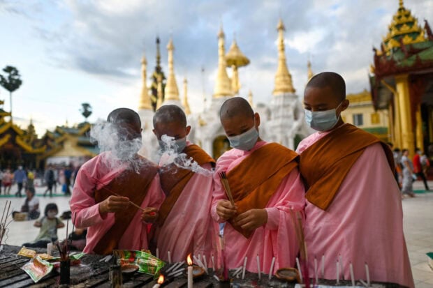 Myanmar monks lighting incense at a temple with golden pagodas in the background