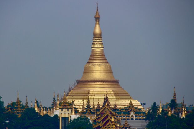 The iconic Myanmar pagoda with golden spires surrounded by lush greenery in a clear sky